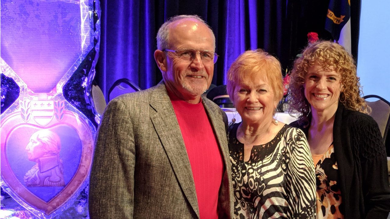 Smiling BodyGuardian Remote Cardiac Monitor patient Bob with two others in front of Purple Heart statue.