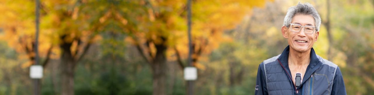 Smiling older man in park wearing BodyGuardian Remote Cardiac Monitor.