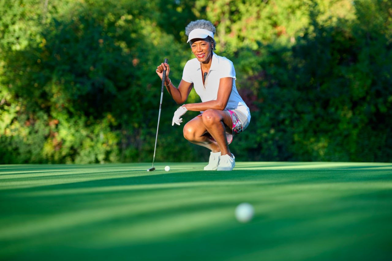 Confident woman crouching on golf course as she wears BodyGuardian MINI remote cardiac monitor.