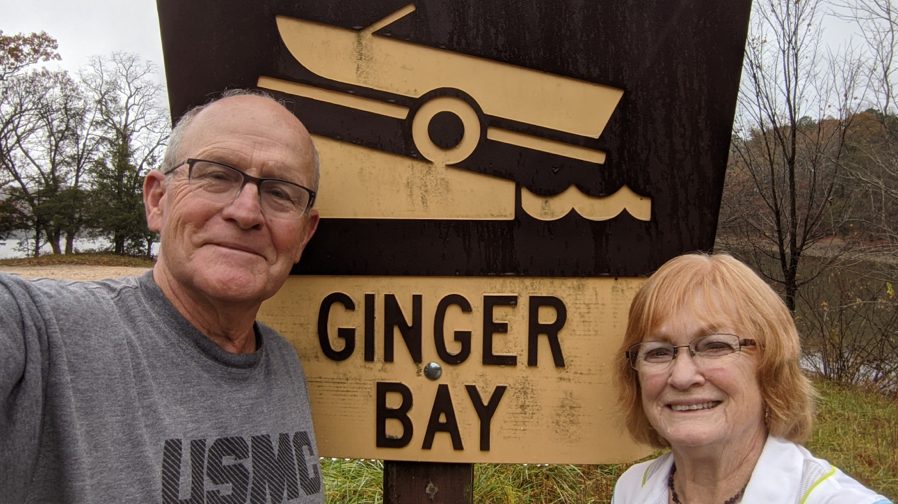 Smiling BodyGuardian Remote Cardiac Monitor patient Bob with a woman in front of a Ginger Bay boat launch sign.