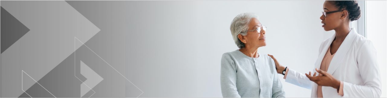 Healthcare professional speaking and touching the shoulder of an older patient.